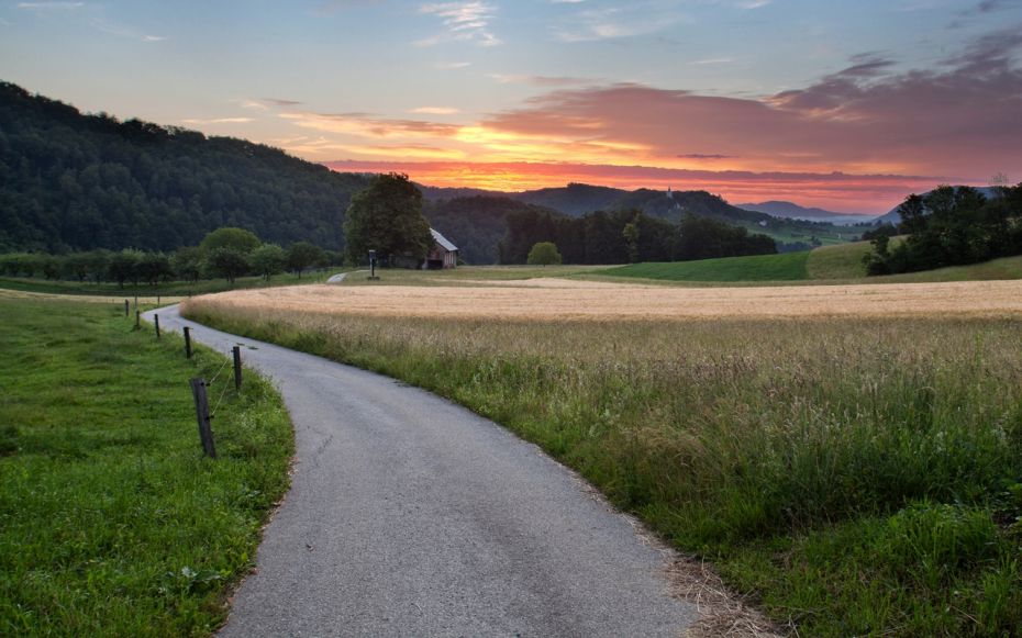 Cesta za kolesarjenje in pohodništvo, ki se vijuga v obzorju. Sproščujoč ambient, sončni zahod.